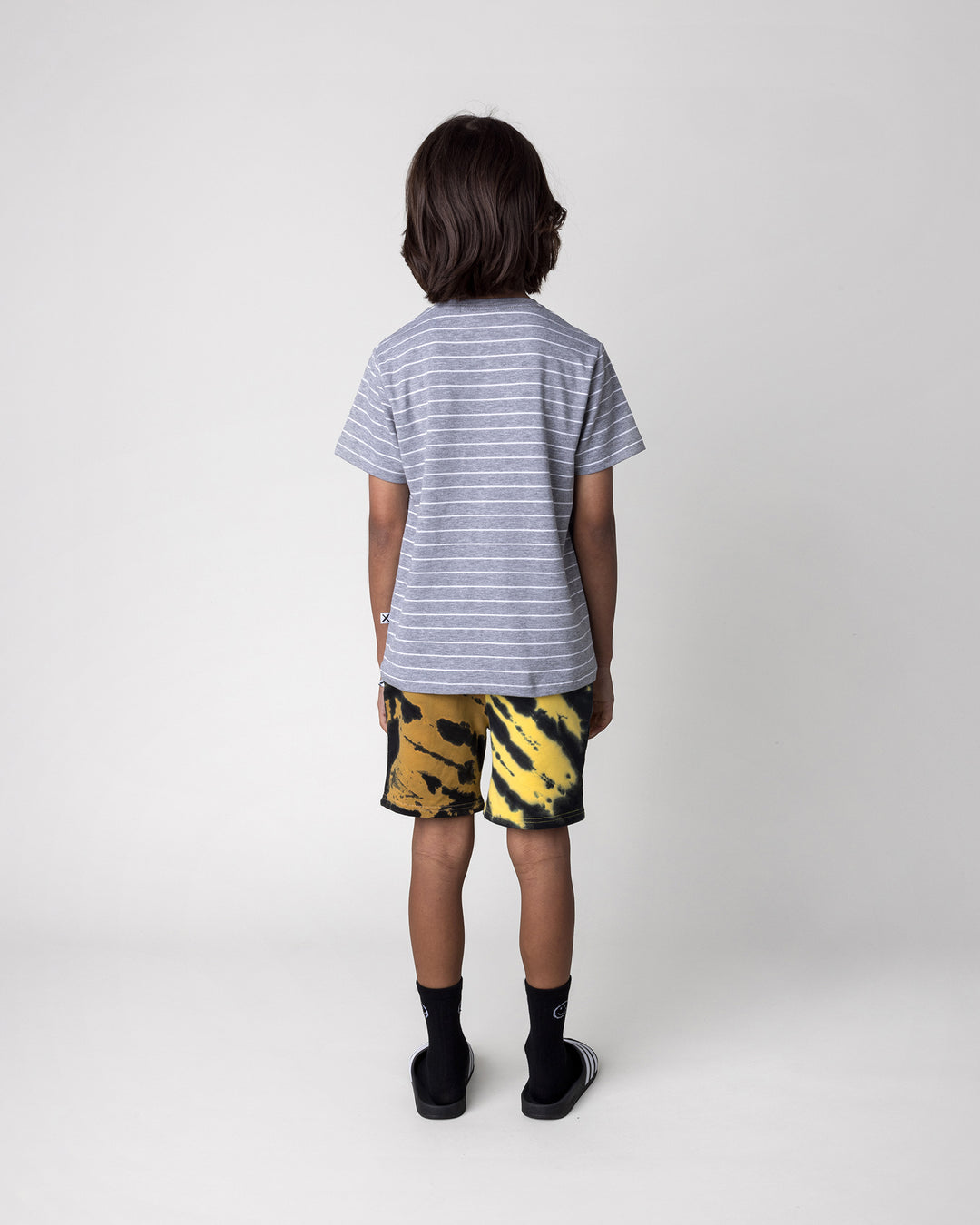Kid wearing the Cool Pterodactyl Tee in grey stripe with the Duo Tie Dye Short in lemon and rust, back view
