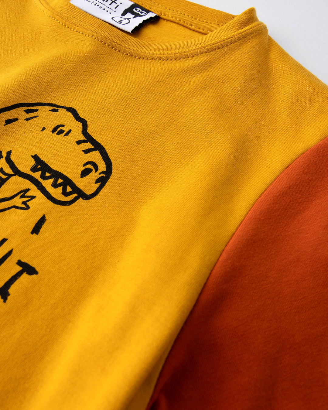 Close up detail of the Dino Ride Tee in mustard, grey and orange