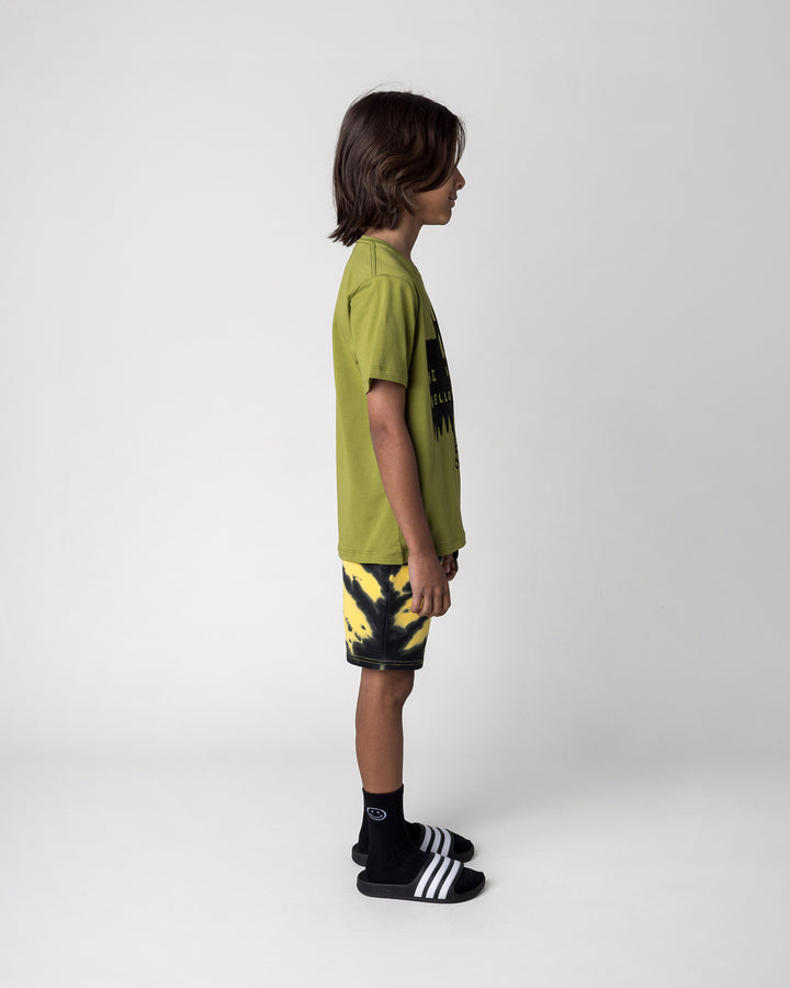 Kid wearing the Greetings Bat Tee in olive with the Duo Tie Dye Short in lemon and rust, side view
