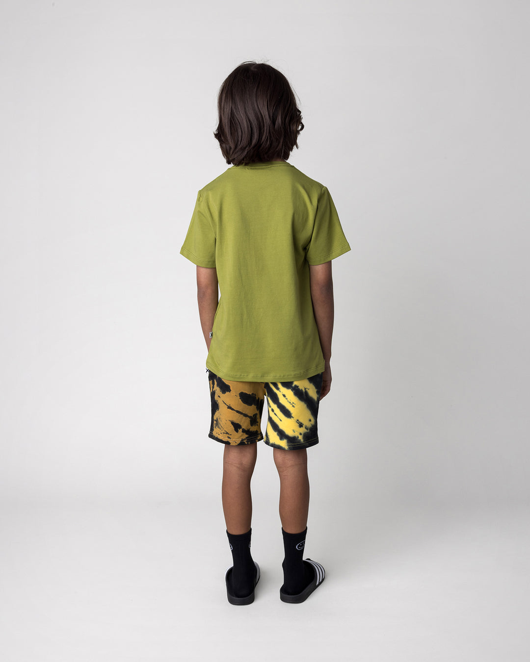 Kid wearing the Greetings Bat Tee in olive with the Duo Tie Dye Short in lemon and rust, back view