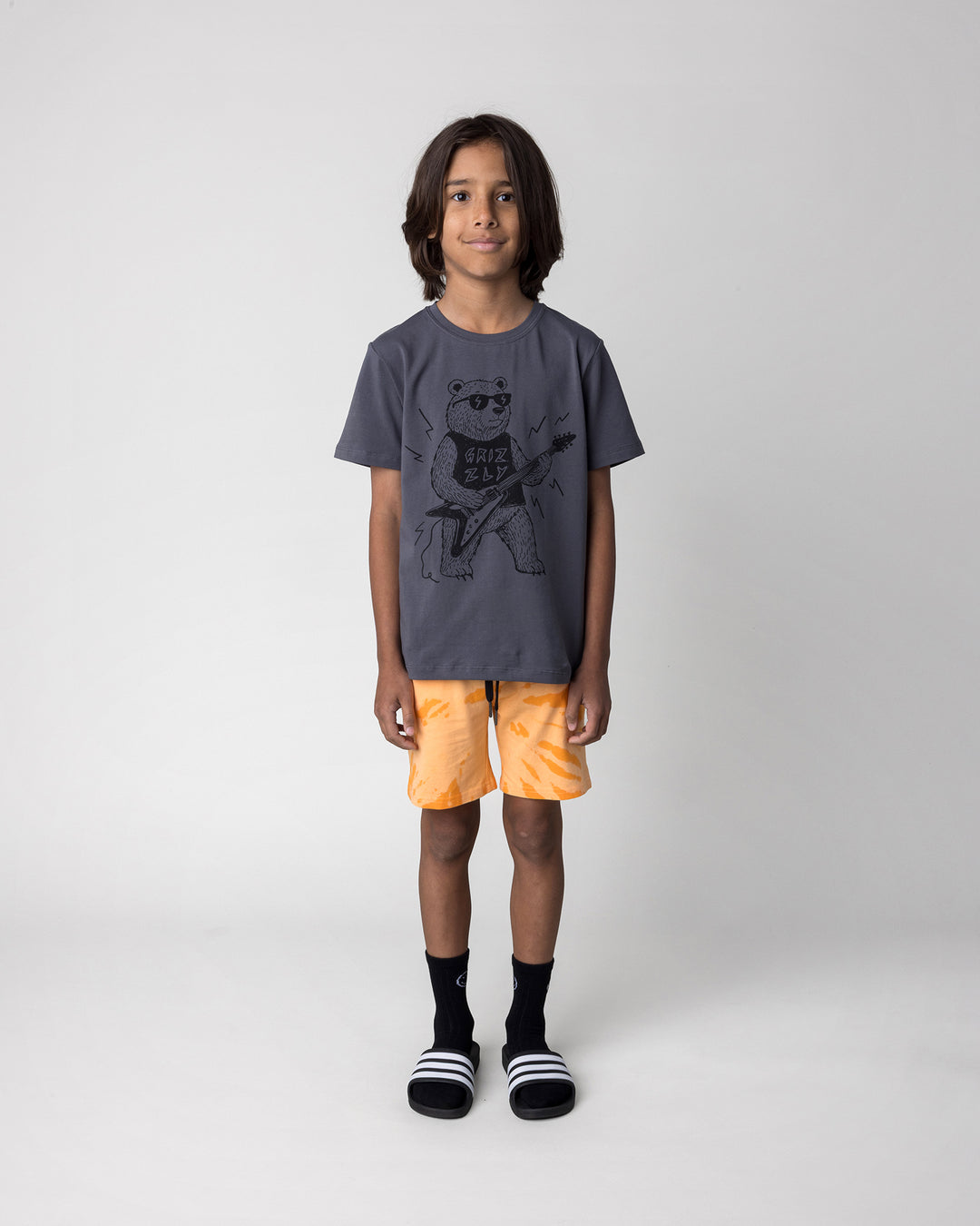 Kid wearing the Grizzly Tee in dark grey with the Splatter Short in orange, front view