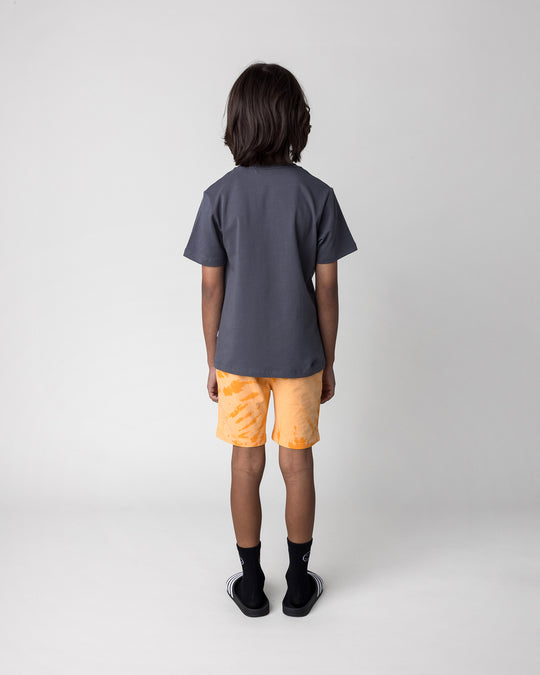 Kid wearing the Grizzly Tee in dark grey with the Splatter Short in orange, back view