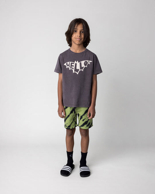 Kid wearing the Hello Bat Tee in black wash with the Strike Short in lime, front view