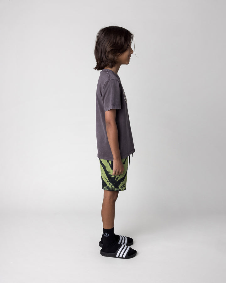 Kid wearing the Hello Bat Tee in black wash with the Strike Short in lime, side view