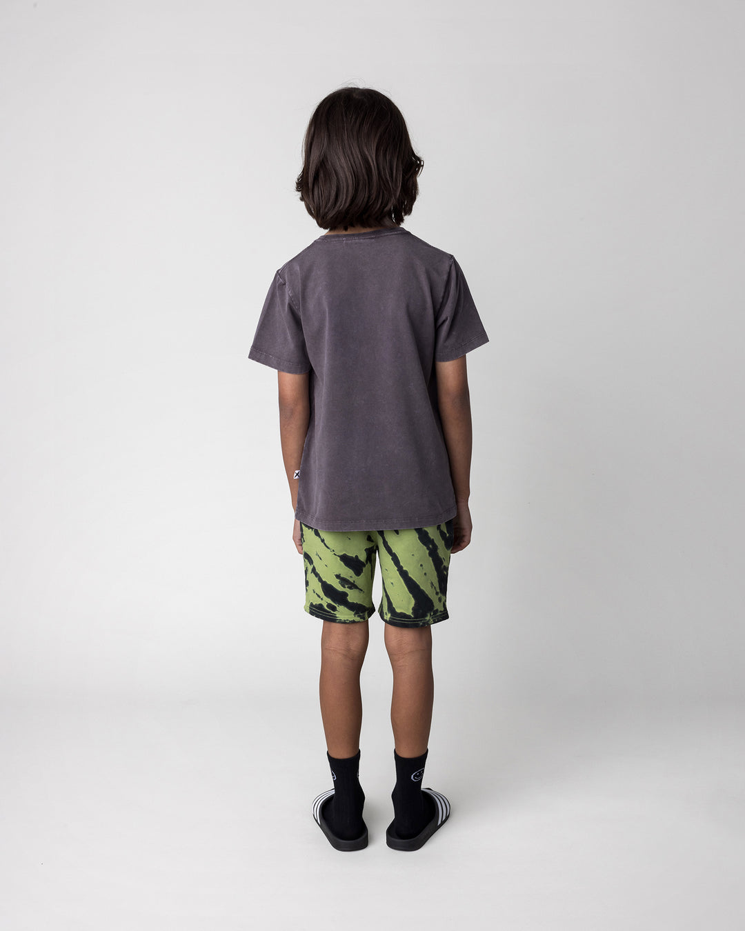 Kid wearing the Hello Bat Tee in black wash with the Strike Short in lime, back view