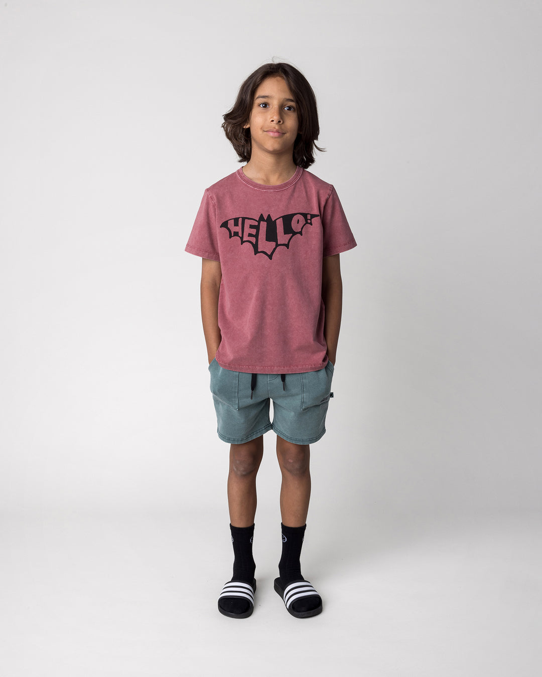 Kid wearing the Hello Bat Tee in burnt red wash with the Blasted Track Short in forest wash, front view