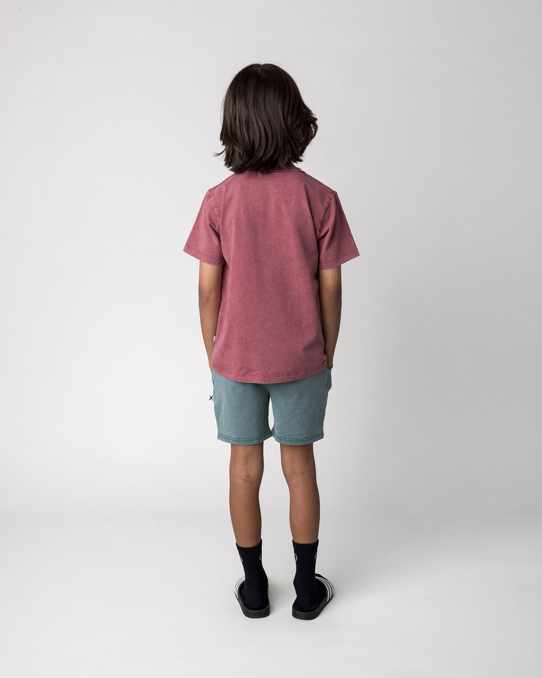 Kid wearing the Hello Bat Tee in burnt red wash with the Blasted Track Short in forest wash, back view