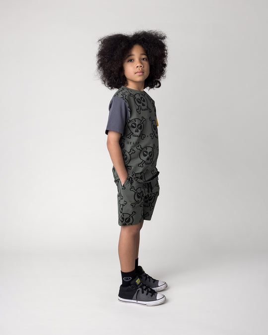 Kid wearing the Hello Skull Tee in forest, dark grey and yellow with the Hello Skull Short in forest, side view