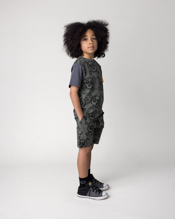 Kid wearing the Hello Skull Tee in forest, dark grey and yellow with the Hello Skull Short in forest, side view