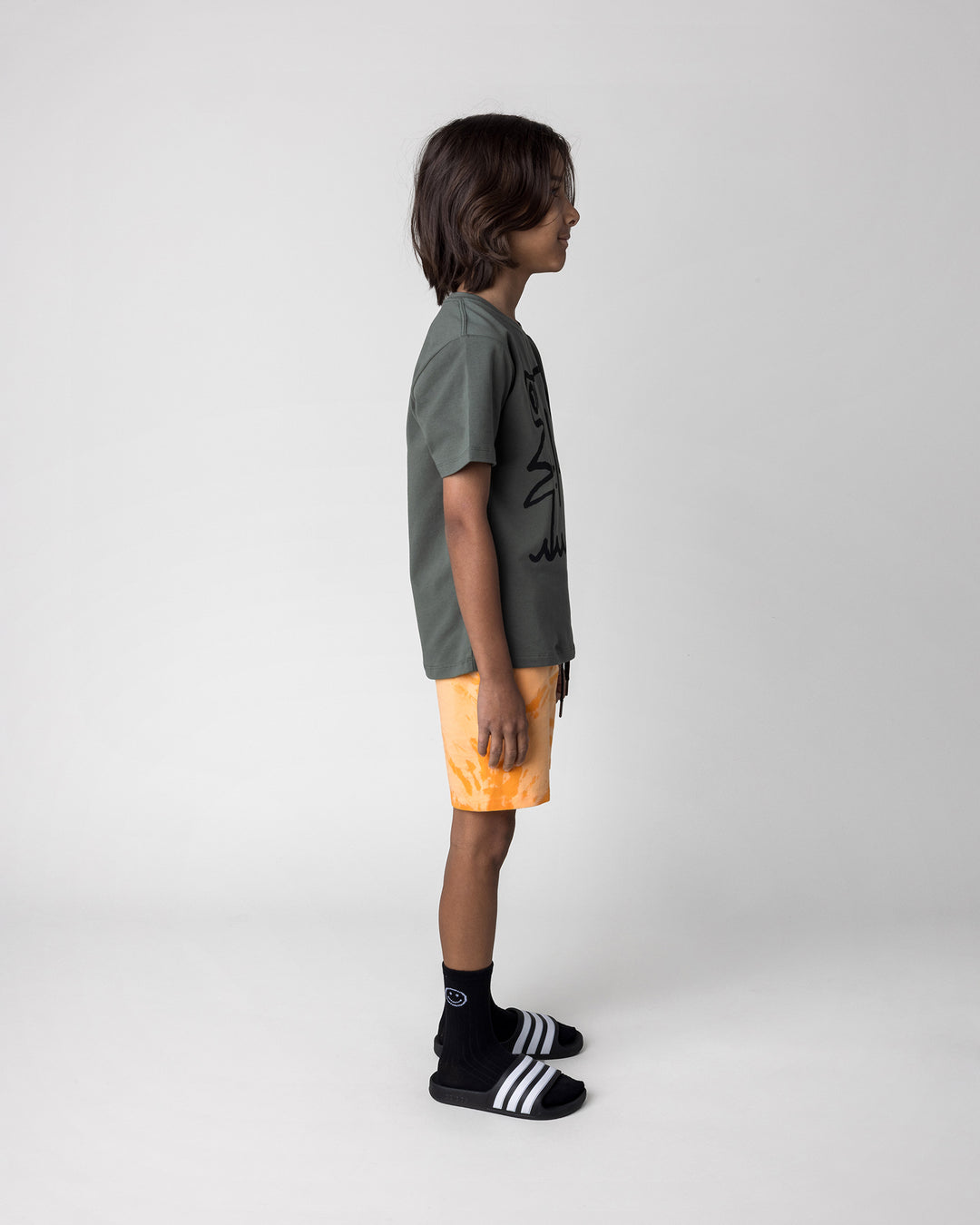 Kid wearing the Hi Hammerhead Tee in forest with the Splatter Short in orange, side view