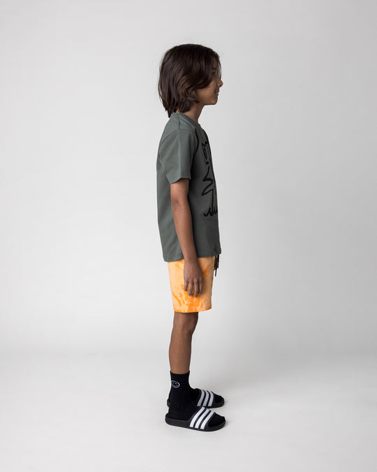 Kid wearing the Hi Hammerhead Tee in forest with the Splatter Short in orange, side view