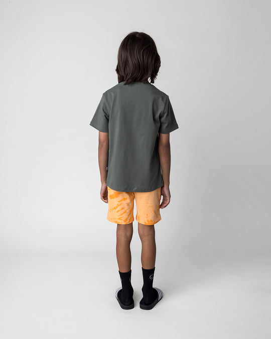 Kid wearing the Hi Hammerhead Tee in forest with the Splatter Short in orange, back view