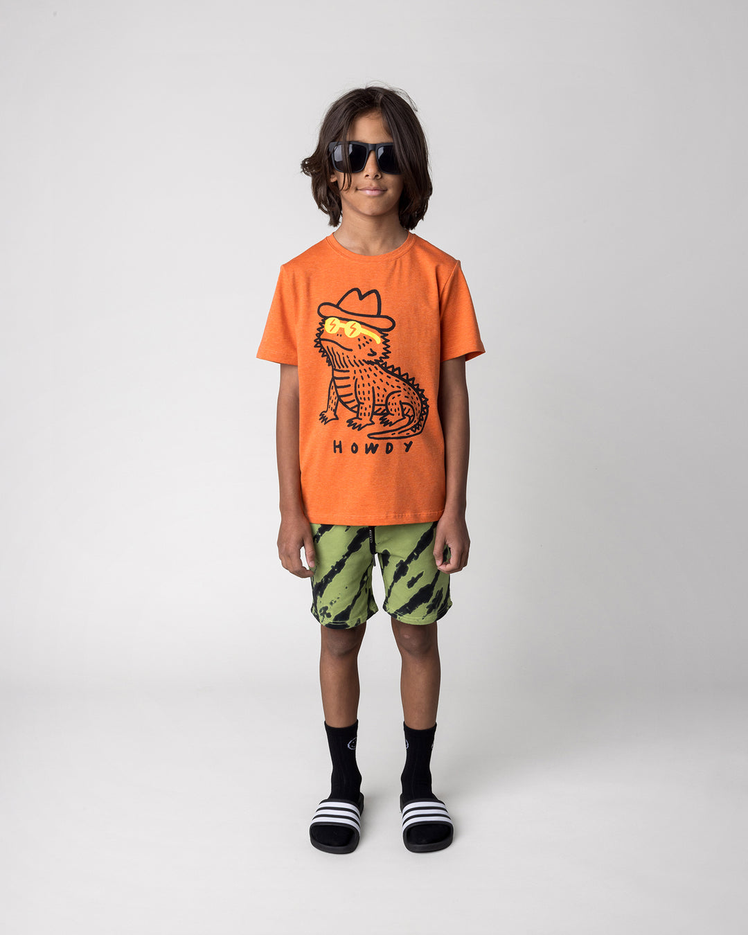 Kid wearing the Howdy Lizard Tee in orange marle with the Strike Short in lime, front view