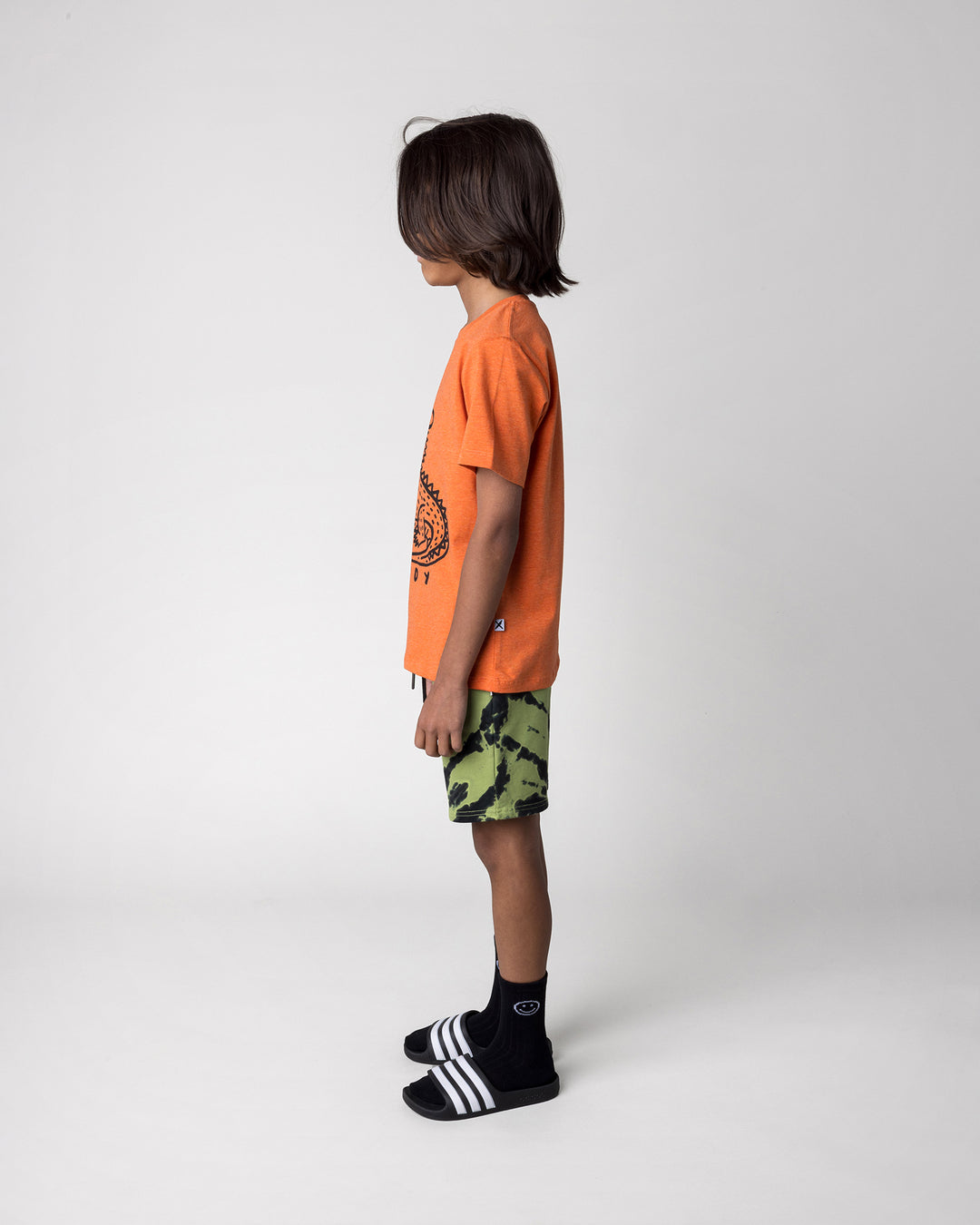 Kid wearing the Howdy Lizard Tee in orange marle with the Strike Short in lime, side view