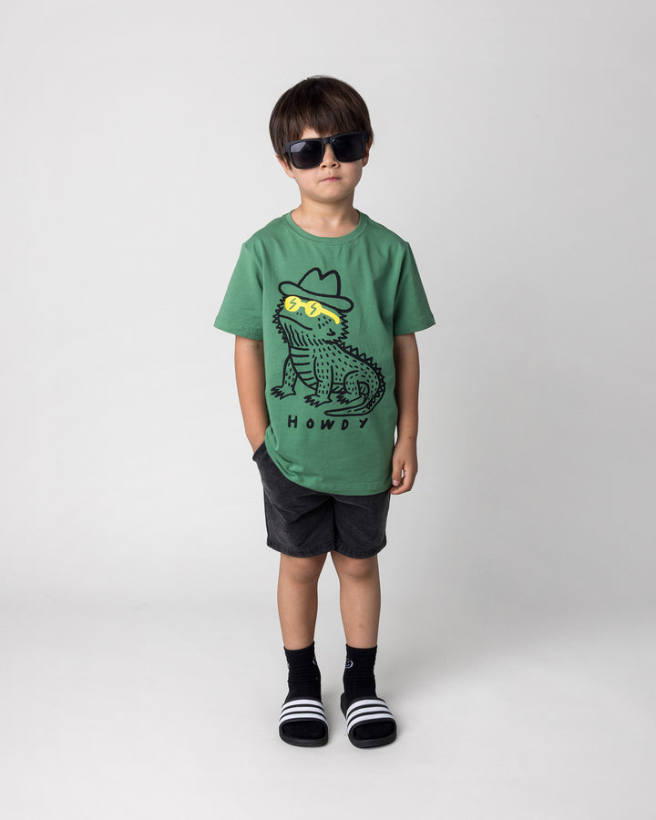 Kid wearing the Howdy Lizard Tee in turf with the Blasted Panel Short in black wash, front view