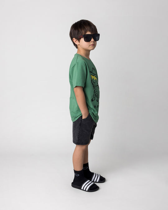 Kid wearing the Howdy Lizard Tee in turf with the Blasted Panel Short in black wash, side view
