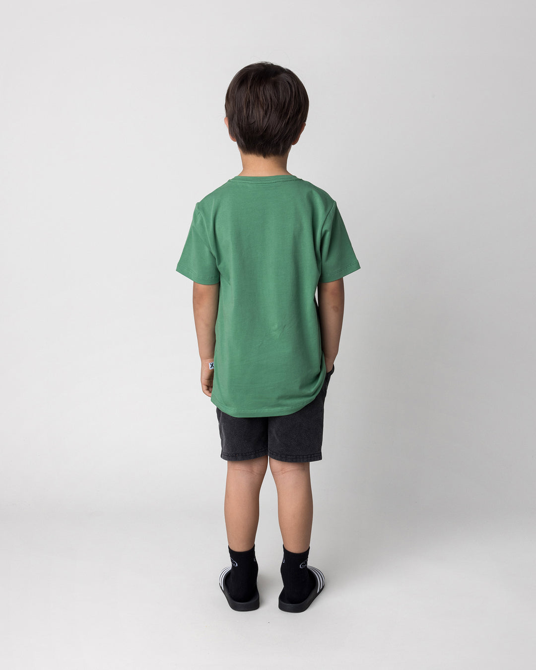 Kid wearing the Howdy Lizard Tee in turf with the Blasted Panel Short in black wash, back view