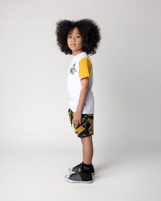 Kid wearing the Hi Pigeon Tee in white, midnight and yellow with the Duo Tie Dye Short in lemon and rust, side view