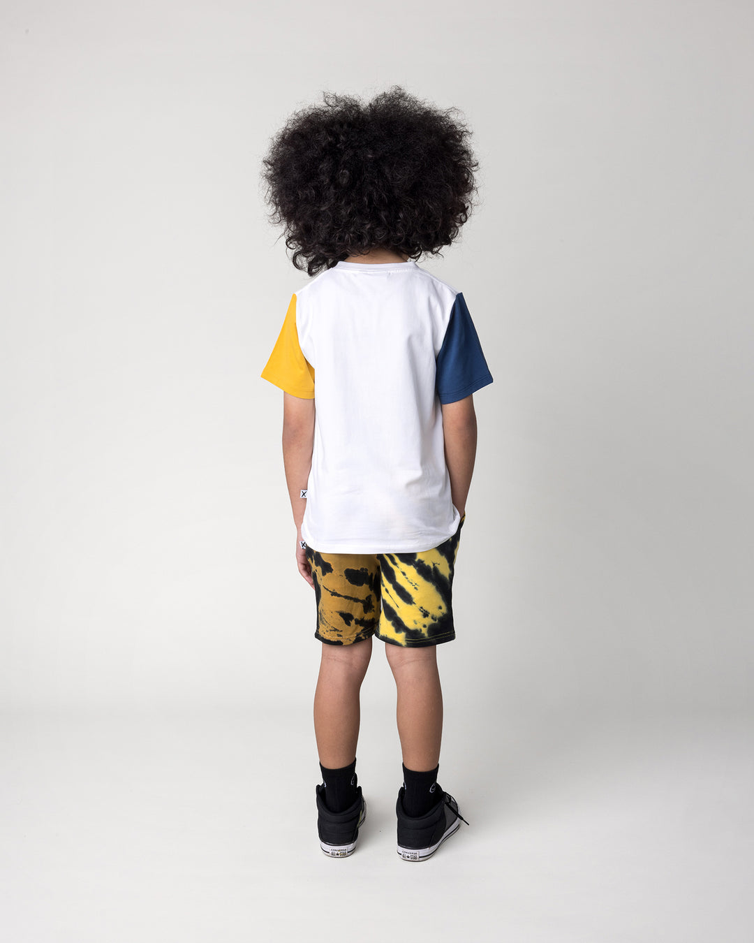 Kid wearing the Hi Pigeon Tee in white, midnight and yellow with the Duo Tie Dye Short in lemon and rust, back view