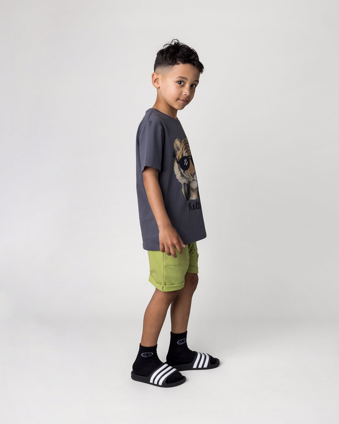 Kid wearing the Headphones Tiger Tee in dark grey with the Roller Short in lime, side view