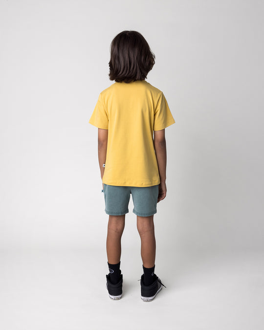 Kid wearing the Headphones Tiger Tee in dull yellow with the Blasted Track Short in forest wash, back view