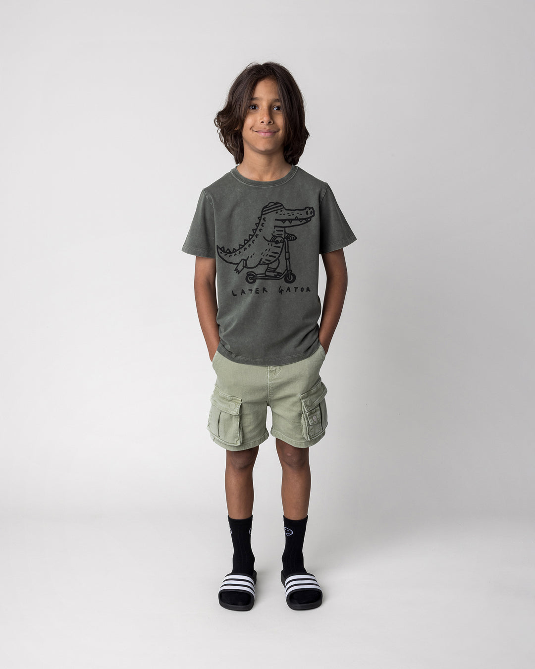 Kid wearing the Later Gator Tee in olive wash, front view