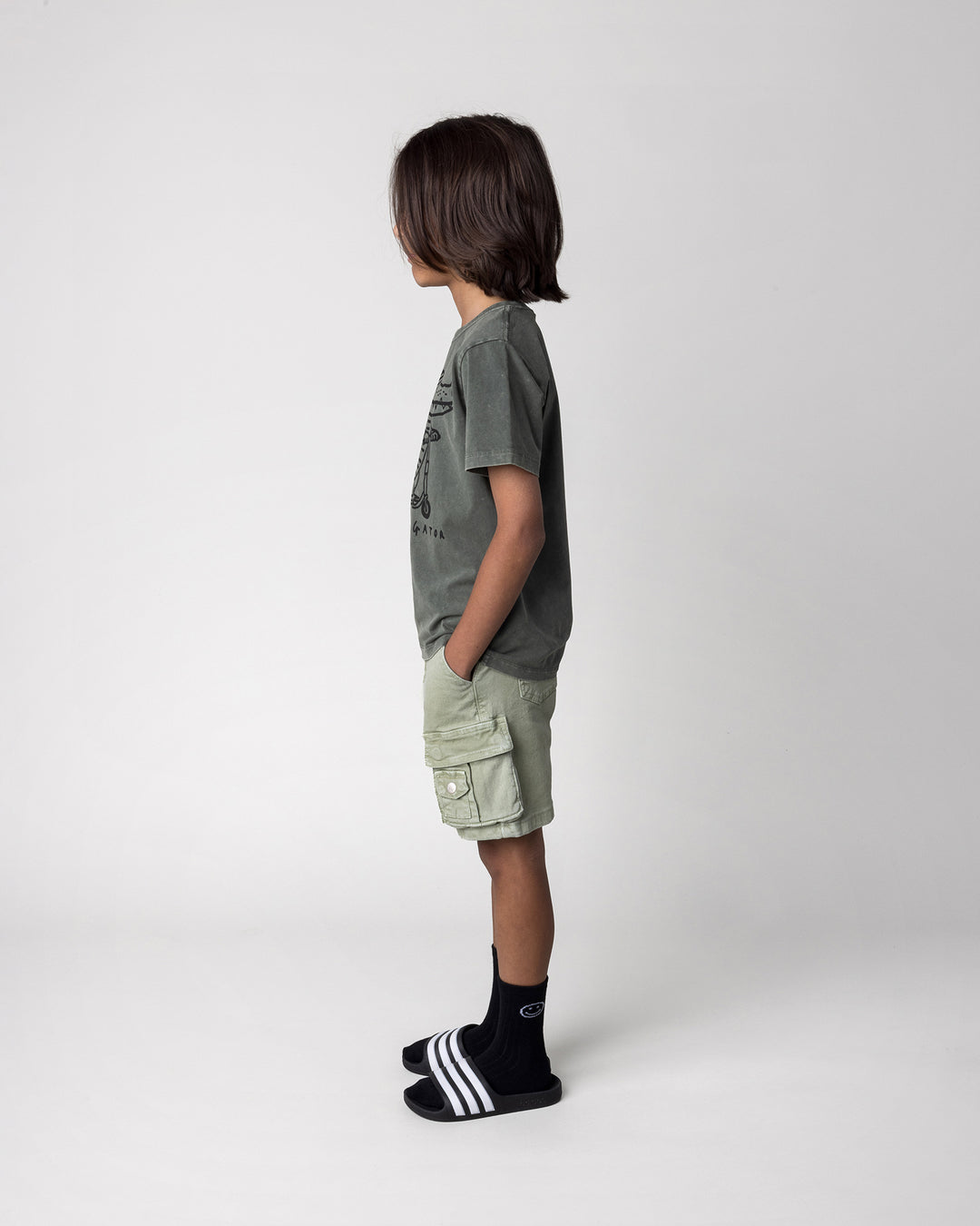 Kid wearing the Later Gator Tee in olive wash, side view