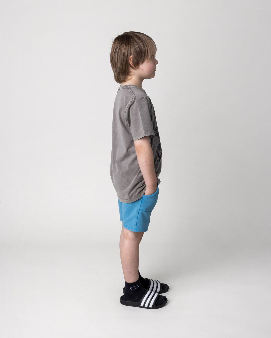 Kid wearing the Mo-Hawk Tee in grey wash with the Blasted Track Short in sky wash, side view