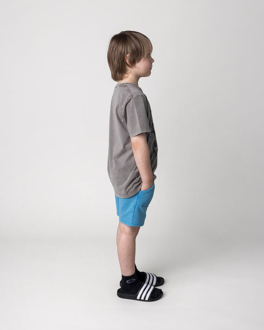 Kid wearing the Mo-Hawk Tee in grey wash with the Blasted Track Short in sky wash, side view