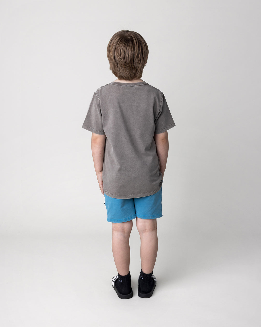 Kid wearing the Mo-Hawk Tee in grey wash with the Blasted Track Short in sky wash, back view