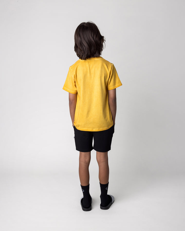 Kid wearing the Mo-Hawk Tee in mustard wash with the Badges Short in black, back view
