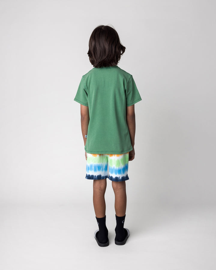 Kid wearing the Patchwork Monster Tee in turf wash with the Airwaves Short in navy, back view
