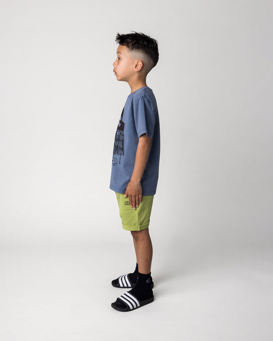 Kid wearing the Pirate Skater Tee in blue wash with the Roller Short in lime, side view