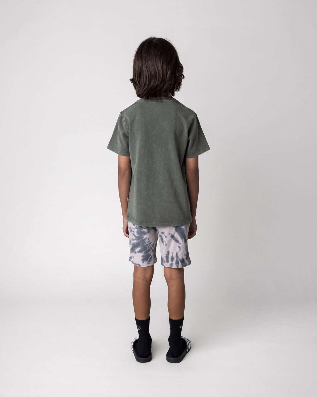 Kid wearing the Radness Tee in olive wash with the Splatter Short in grey, back view
