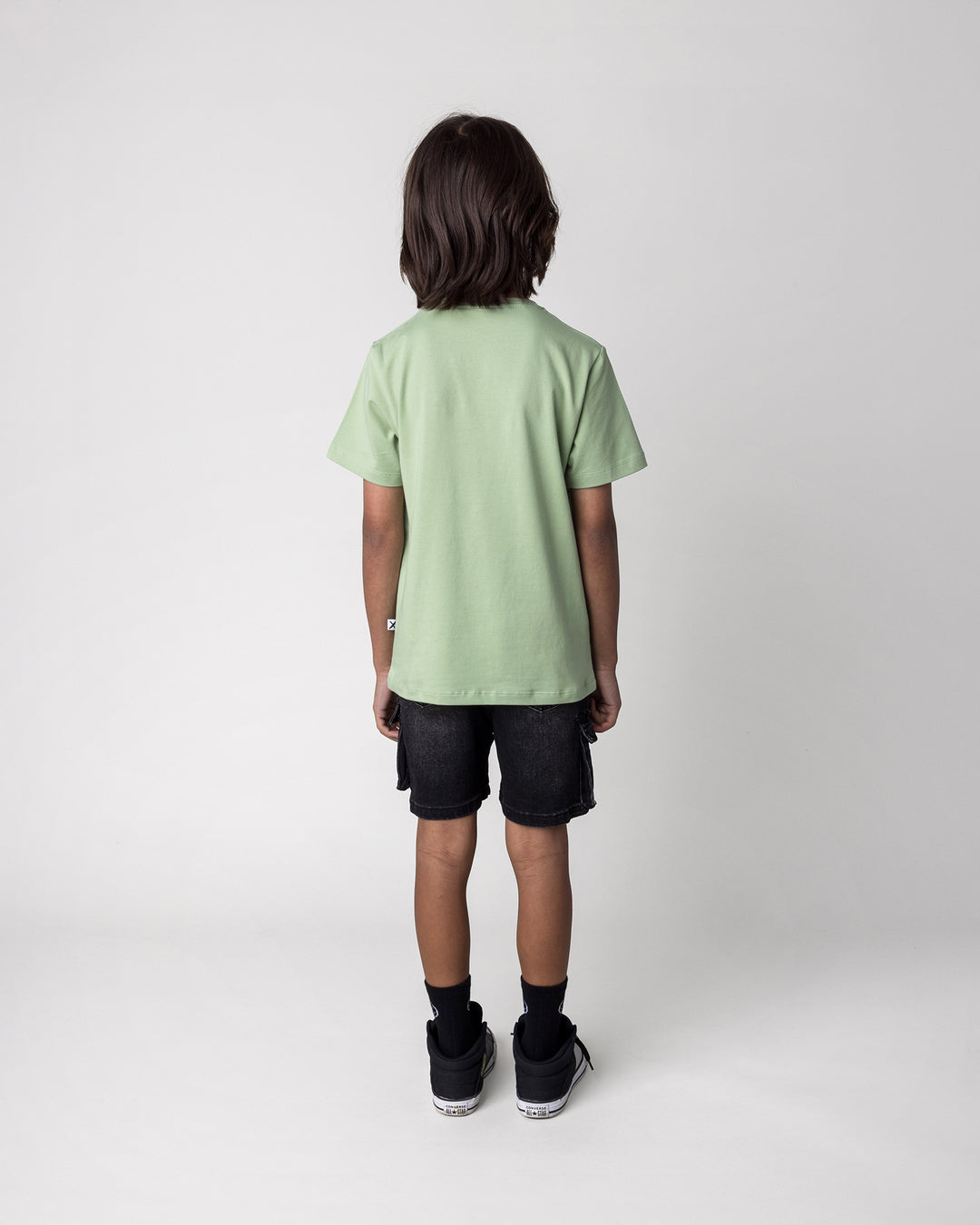 Kid wearing the Rex Rider Tee in sage, back view