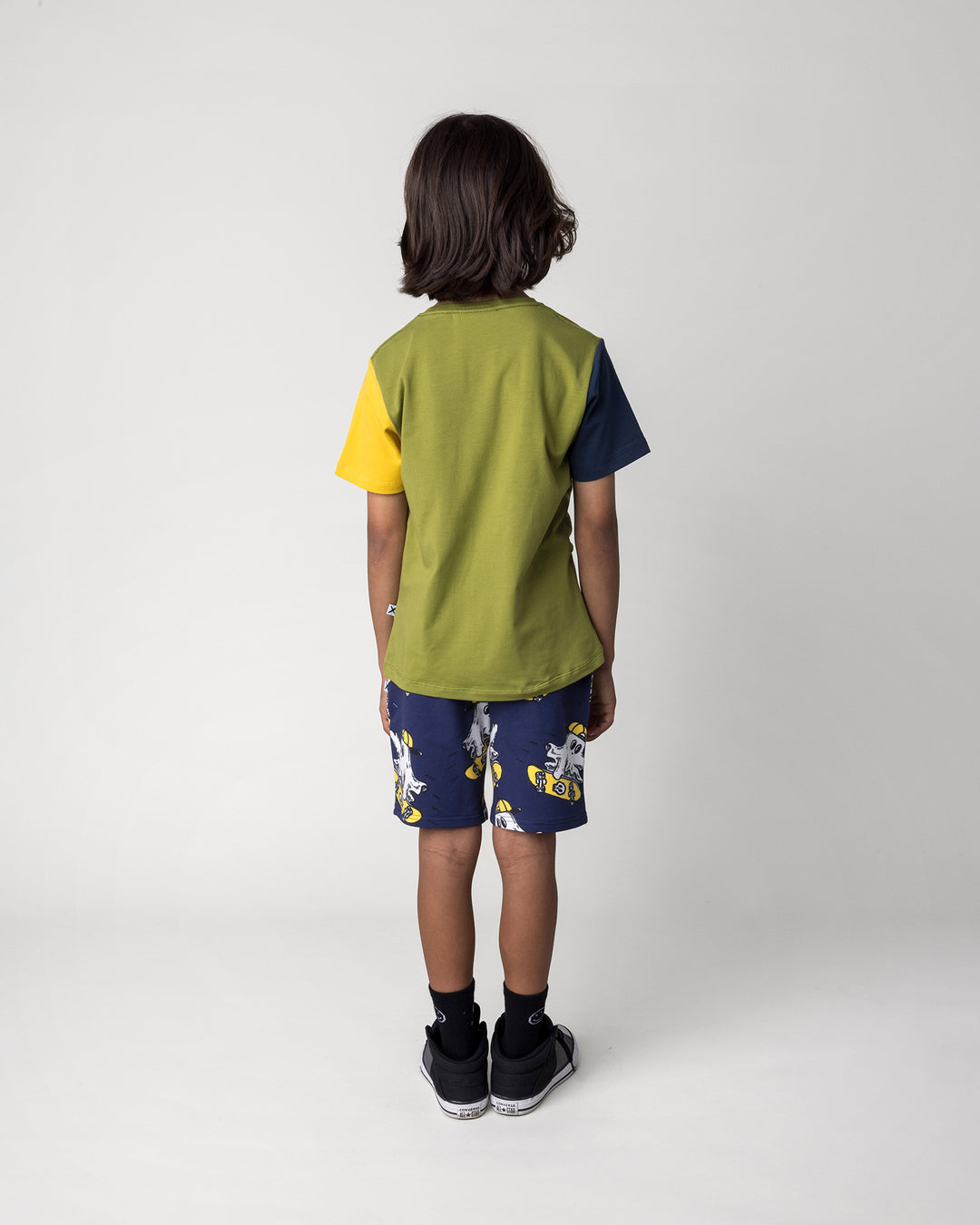 Kid wearing the Skate Ghost Tee in olive, ink and mustard with the Skate Ghost Short in dark blue, back view