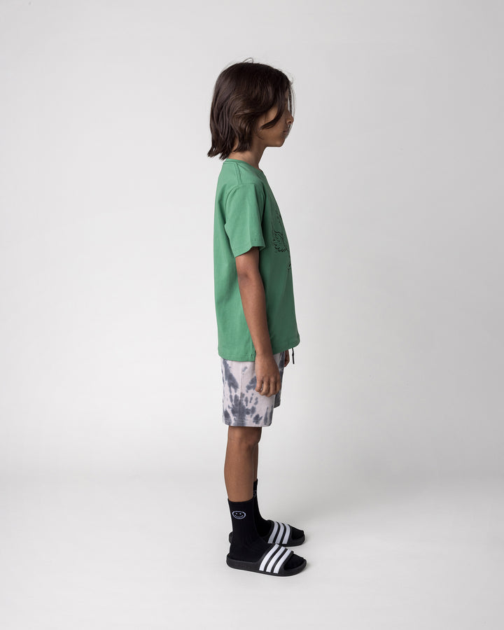 Kid wearing the Skate Phoenix Tee in turf with the Splatter Short in grey, side view