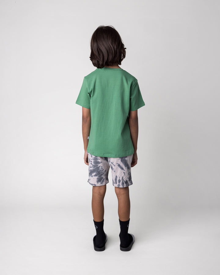 Kid wearing the Skate Phoenix Tee in turf with the Splatter Short in grey, back view