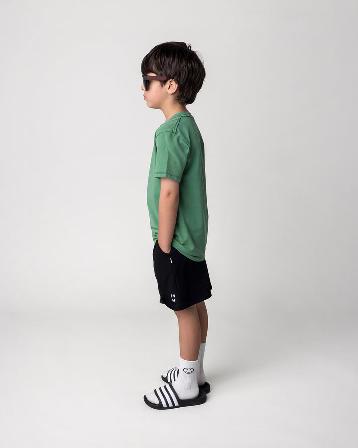 Kid wearing the Super Cool Tee in turf wash with the Smile Short in black, side view