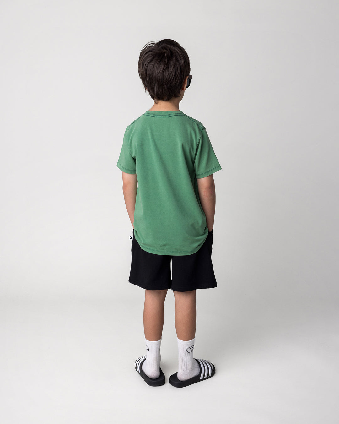 Kid wearing the Super Cool Tee in turf wash with the Smile Short in black, back view