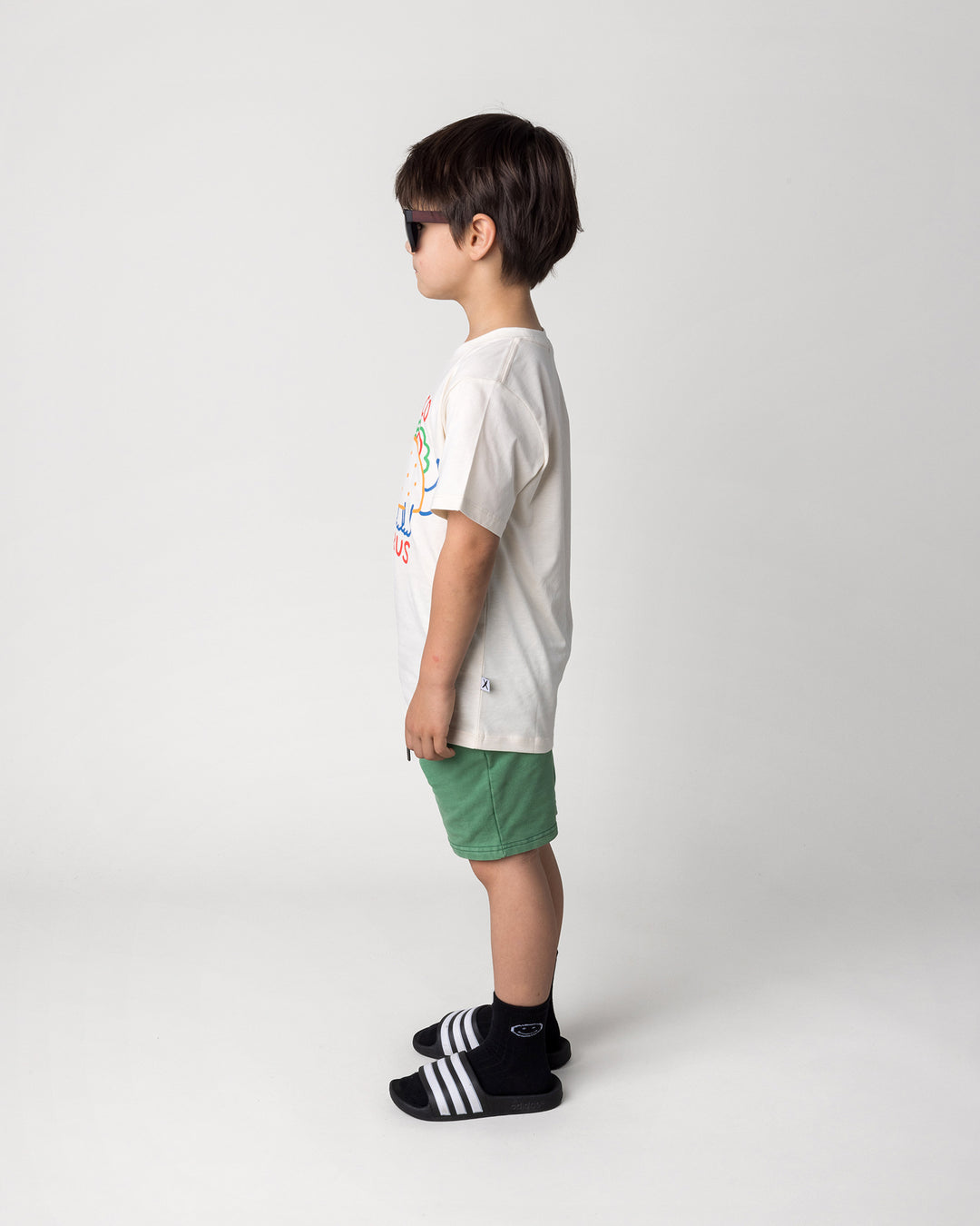 Kid wearing the Taco Saurus Tee in cream with the Blasted Icon Short in turf wash, side view