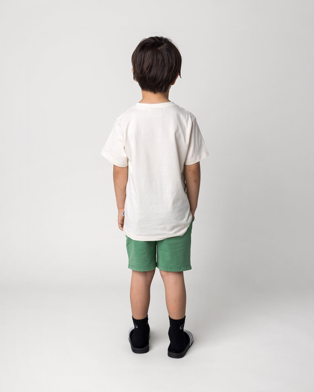 Kid wearing the Taco Saurus Tee in cream with the Blasted Icon Short in turf wash, back view