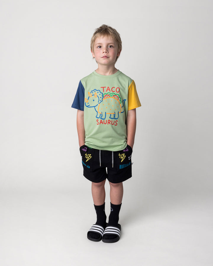 Kid wearing the Taco Saurus Tee in sage, midnight and yellow with the Badges Short in black, front view