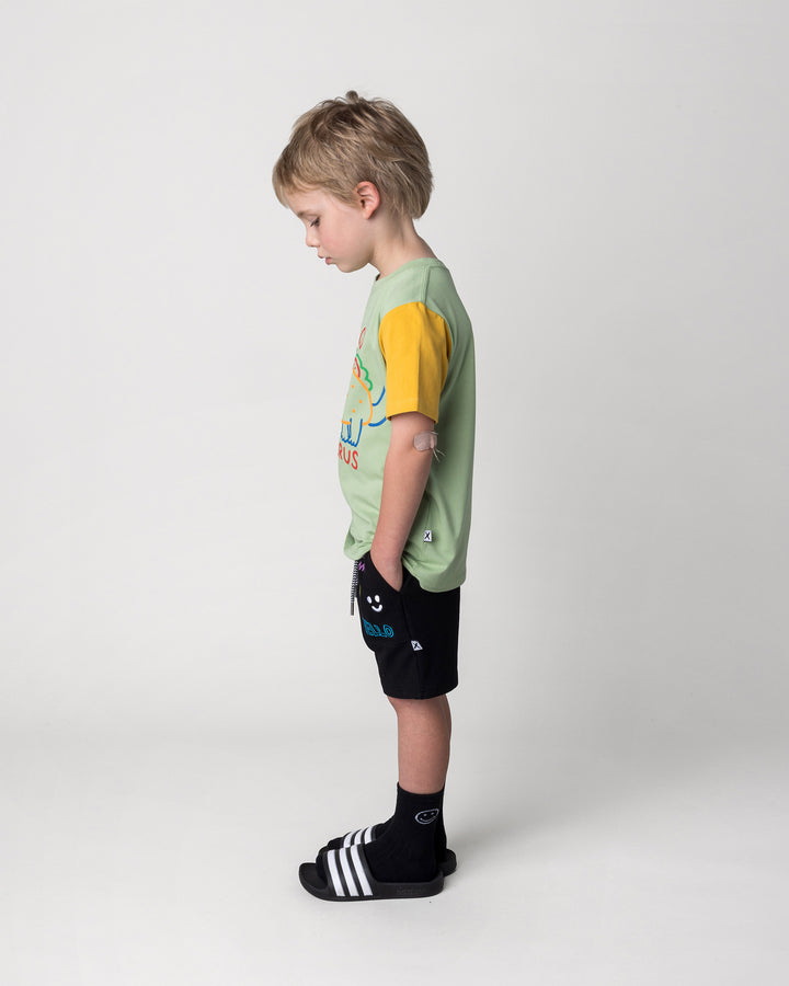 Kid wearing the Taco Saurus Tee in sage, midnight and yellow with the Badges Short in black, side view