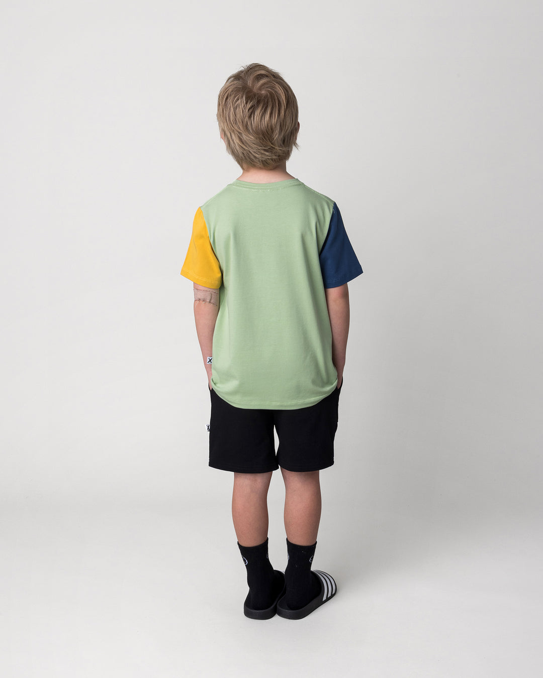 Kid wearing the Taco Saurus Tee in sage, midnight and yellow with the Badges Short in black, back view