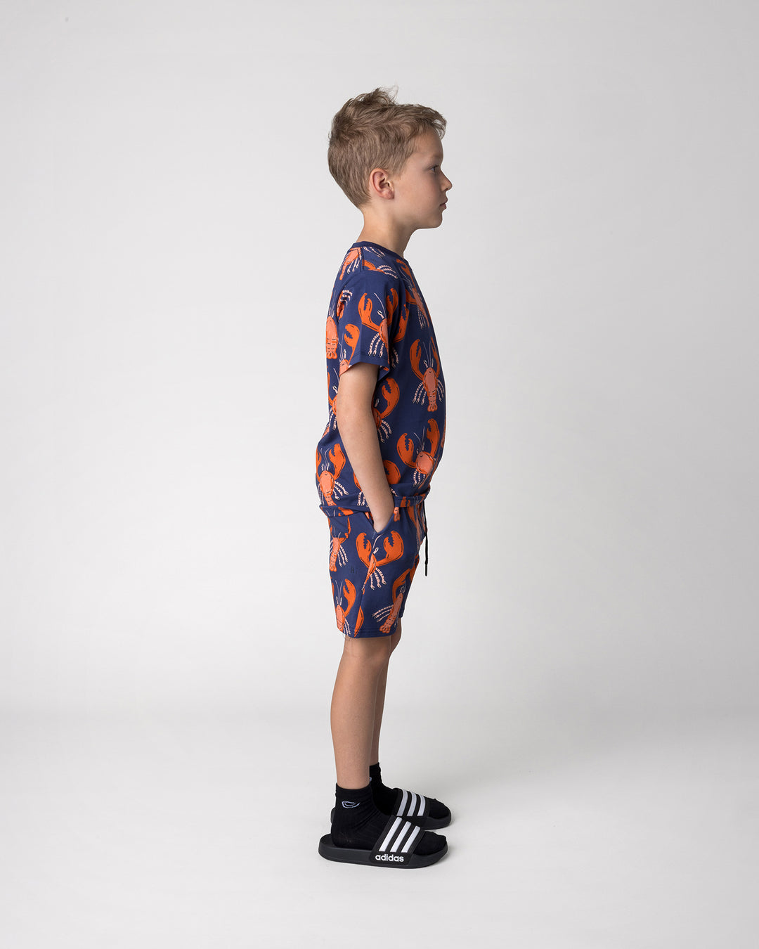 Kid wearing the Vacay Crayfish Tee in midnight with the Vacay Crayfish Short in midnight, side view