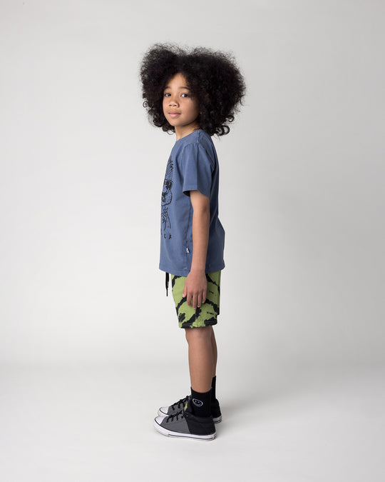 Kid wearing the Werewolf Rockstar Tee in blue wash with the Strike Short in lime, side view