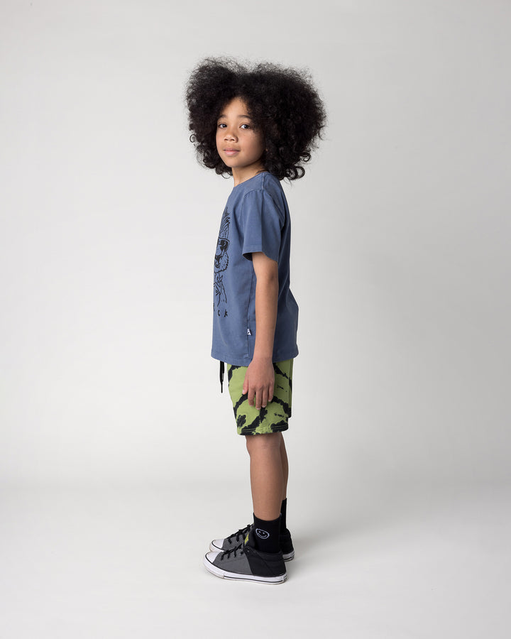 Kid wearing the Werewolf Rockstar Tee in blue wash with the Strike Short in lime, side view