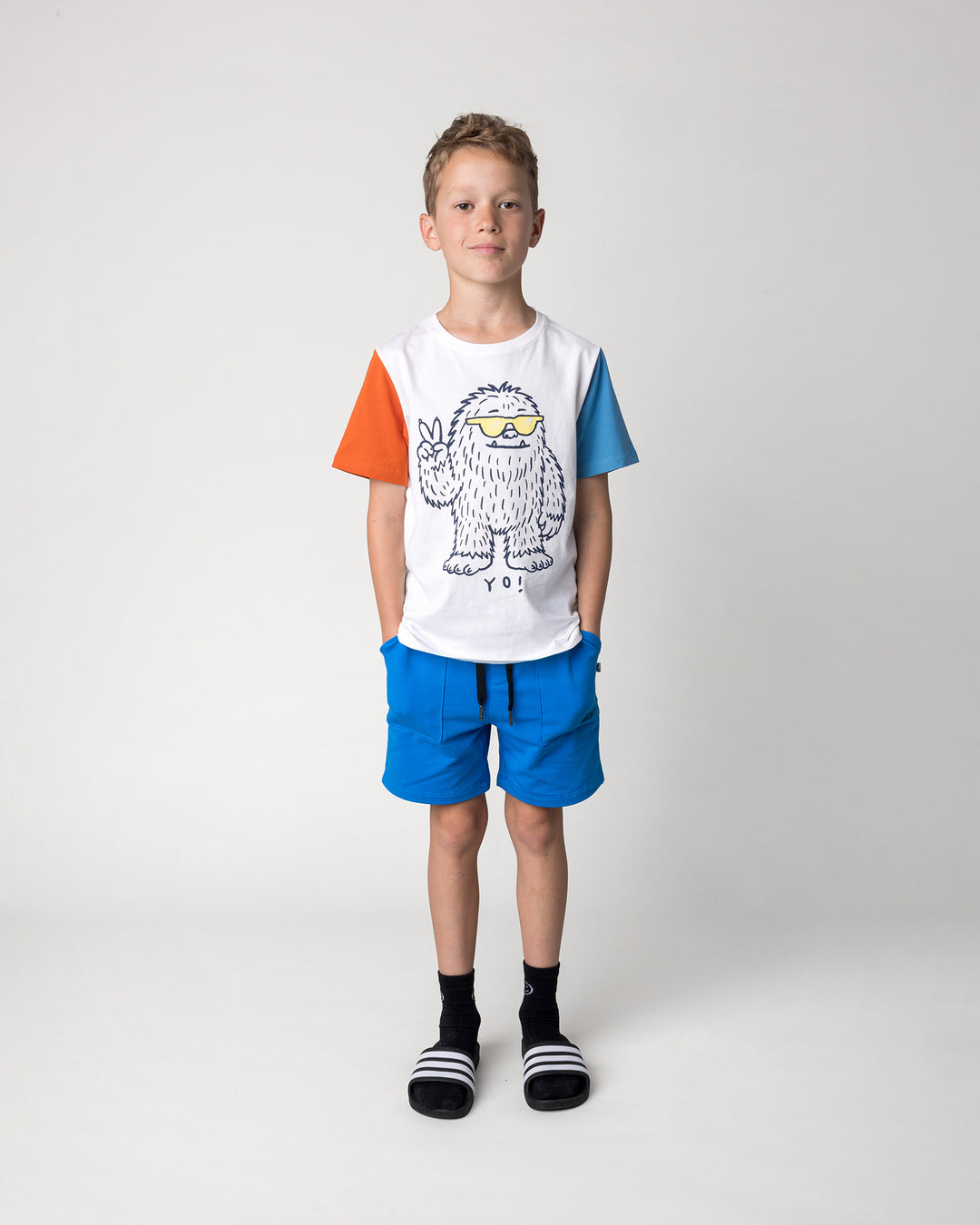 Kid wearing the Yo Yeti Tee in white, orange and steel with the Track Short in cobalt, front view