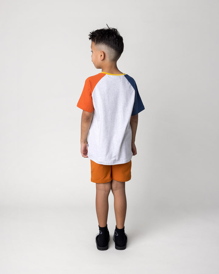 Kid wearing the Cool Pterodactyl Tee in white marle and multi with the Track Short in burnt orange, back view